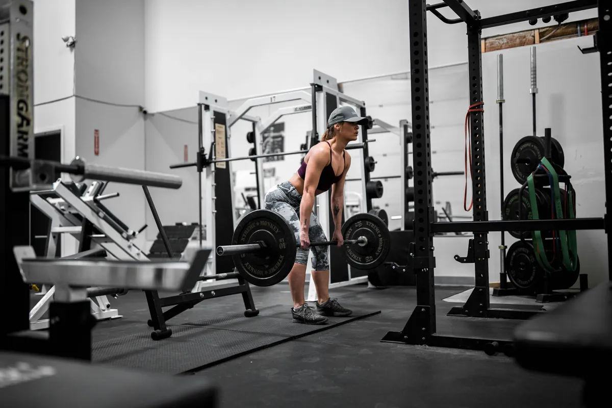 A lifter at the top of a deadlift in a gym, a loaded barbell in both hands